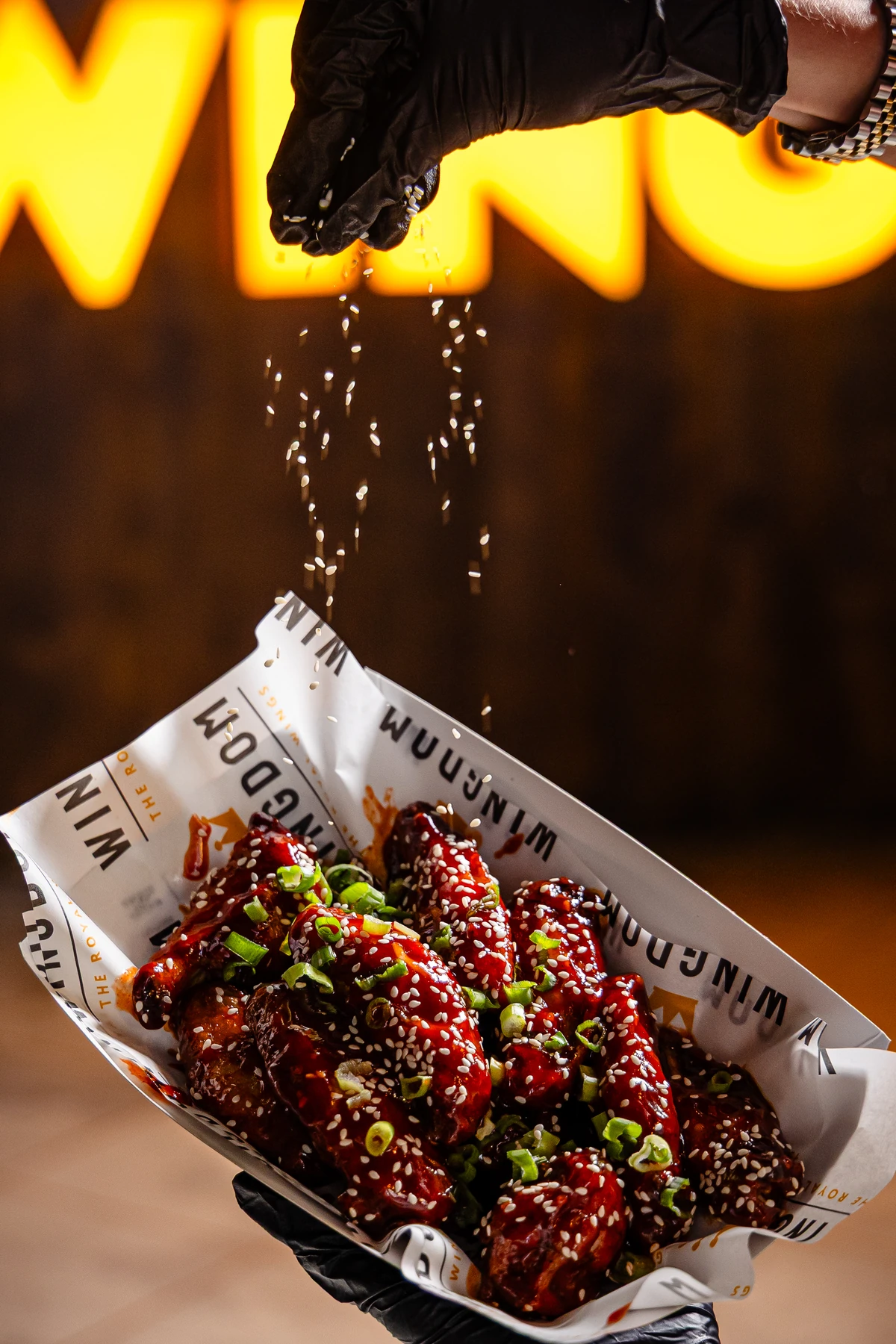 A Wingdom team member finishing glazed wings with sesame seeds